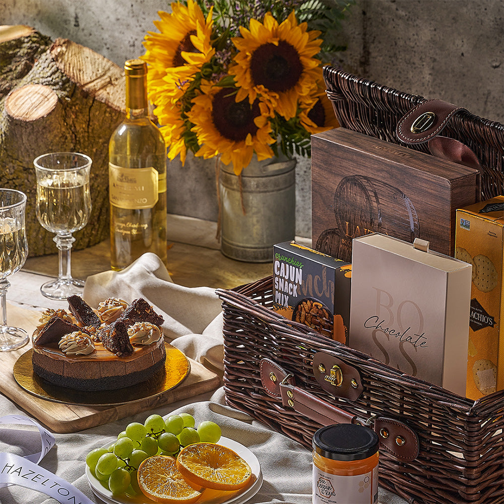 Gourmet picnic setup with a cake, wine, sunflowers, and snacks on a wooden table.